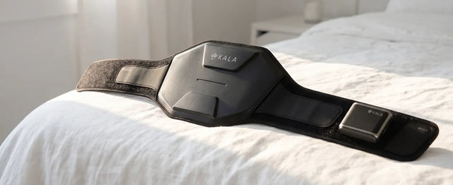 KALA red light therapy belt and portable controller resting on a white bed in a bright, modern bedroom.
