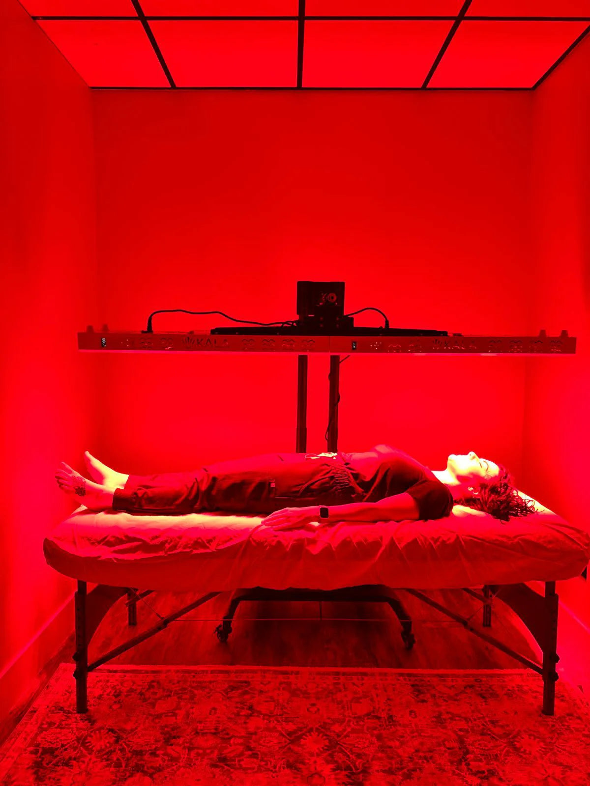 Person lying on a bed in a room with kala red light duo panel and lighting.