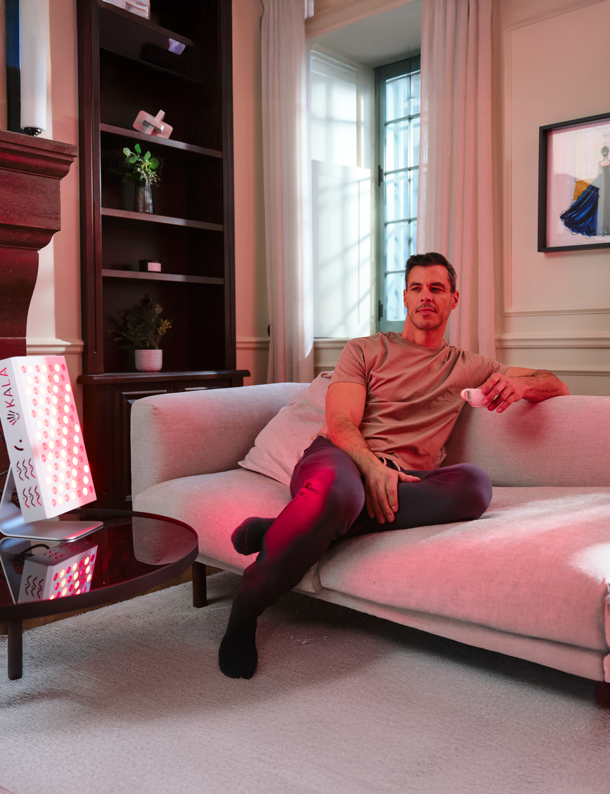 Man sitting on a couch in a living room with Kala Red Light Pro Panel delivers professional-grade red and near-infrared therapy for half-body coverage.