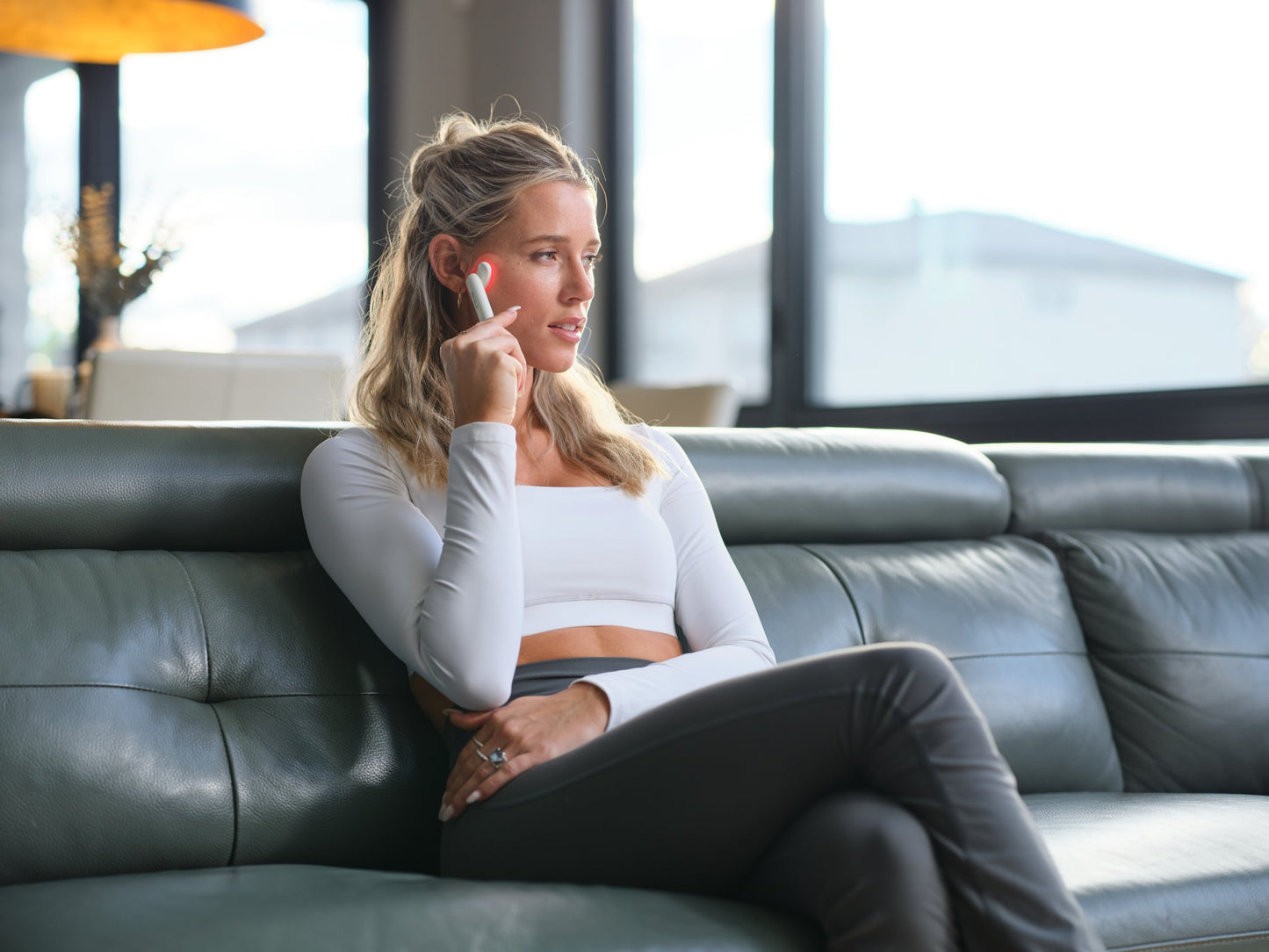 Woman sitting on a leather couch using Kala Therapy Wand is a compact, medical-grade device designed to deliver gentle red and blue light therapy directly where you need it most.