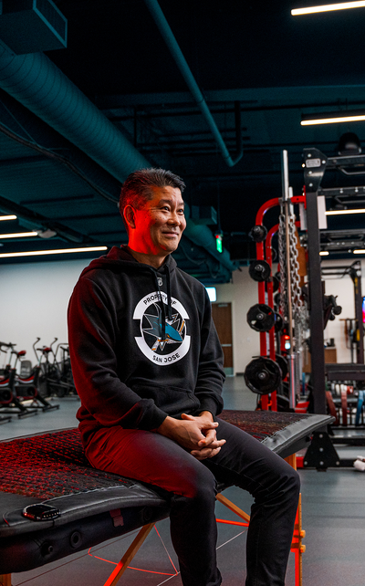 A man wearing a San Jose Sharks hoodie sitting on a specialized treatment table equipped with a Kala red light therapy mat inside an athletic training facility.