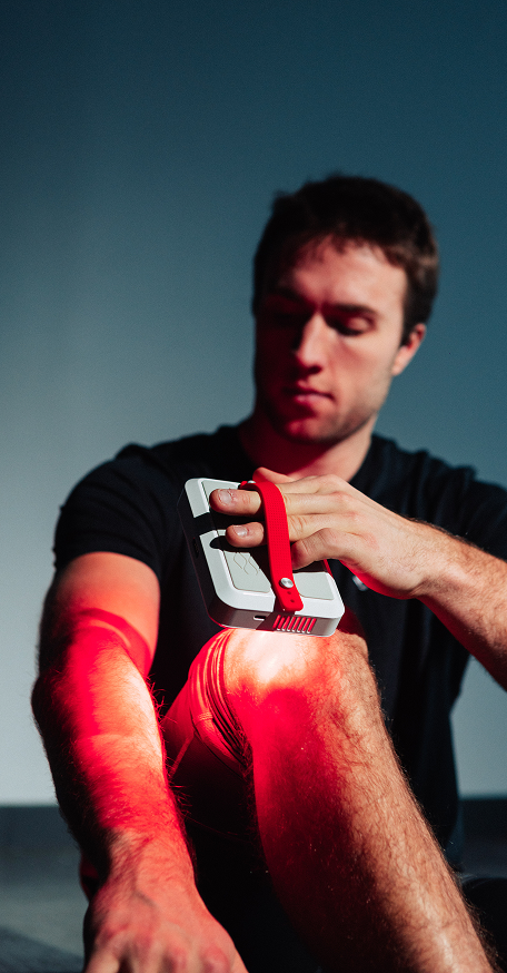 Close-up of a compact Kala red light therapy device being applied directly to the knee for localized muscle and joint recovery.