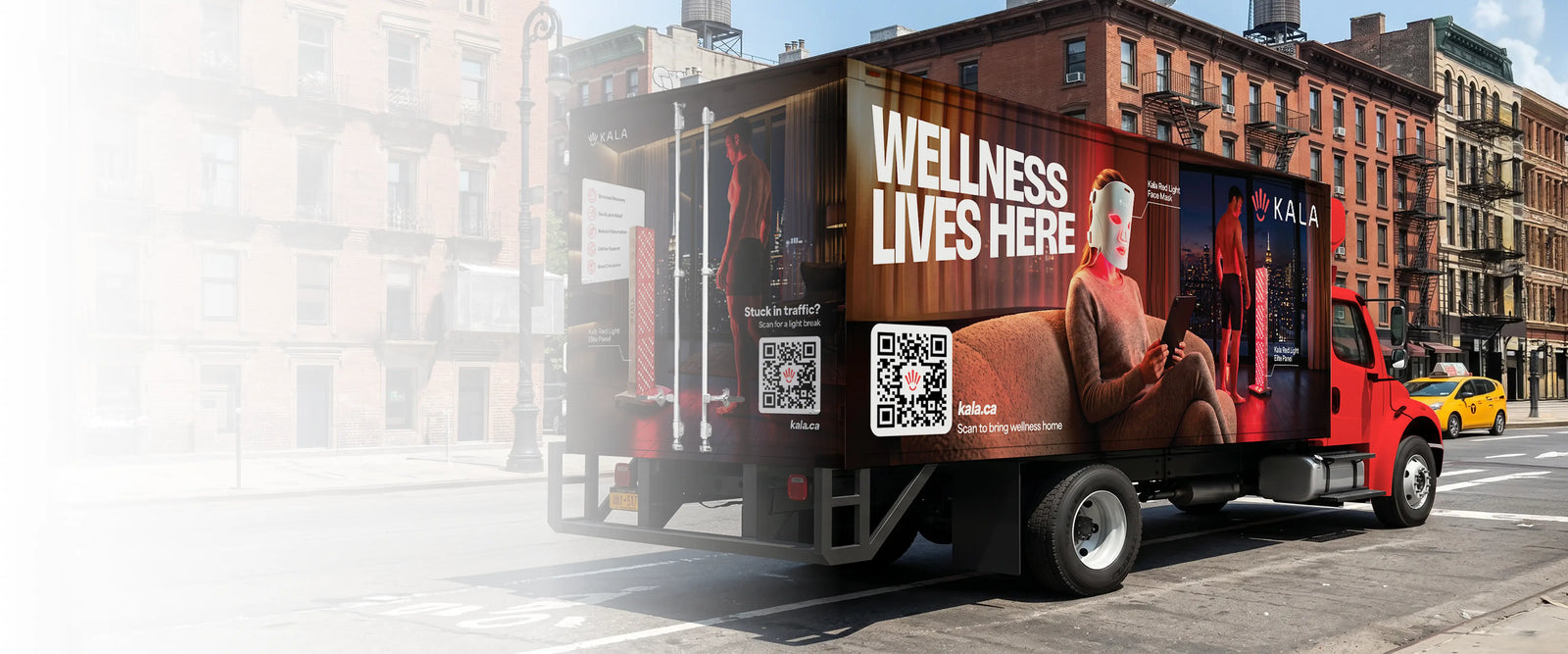 A red delivery truck parked on a city street, featuring a large wellness advertisement on its side with the text 'WELLNESS LIVES HERE' and a photo of a woman meditating. The background shows blurred brick buildings and a yellow taxi.