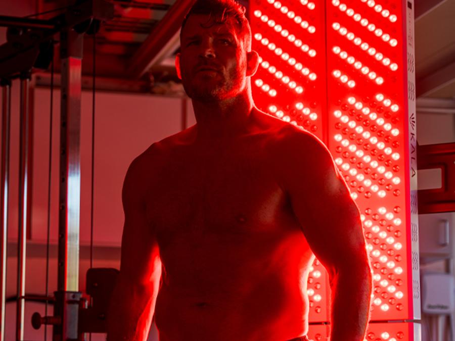 Kala in front of a red light therapy panel in a gym setting