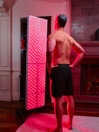 Man standing in front of a kala red light therapy panel in a room with a fireplace.
