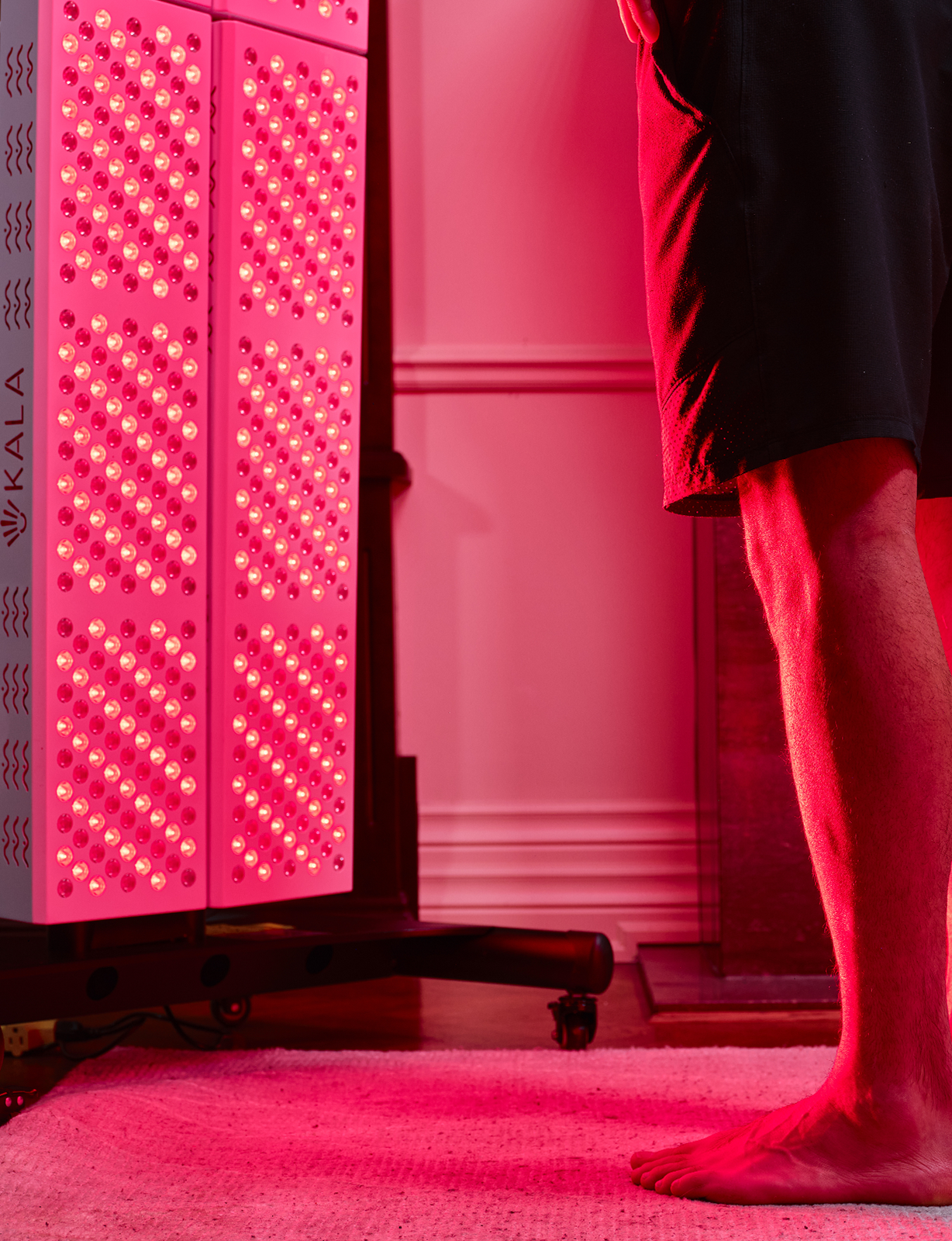 Person standing next to a Kala LED light therapy device in a room.