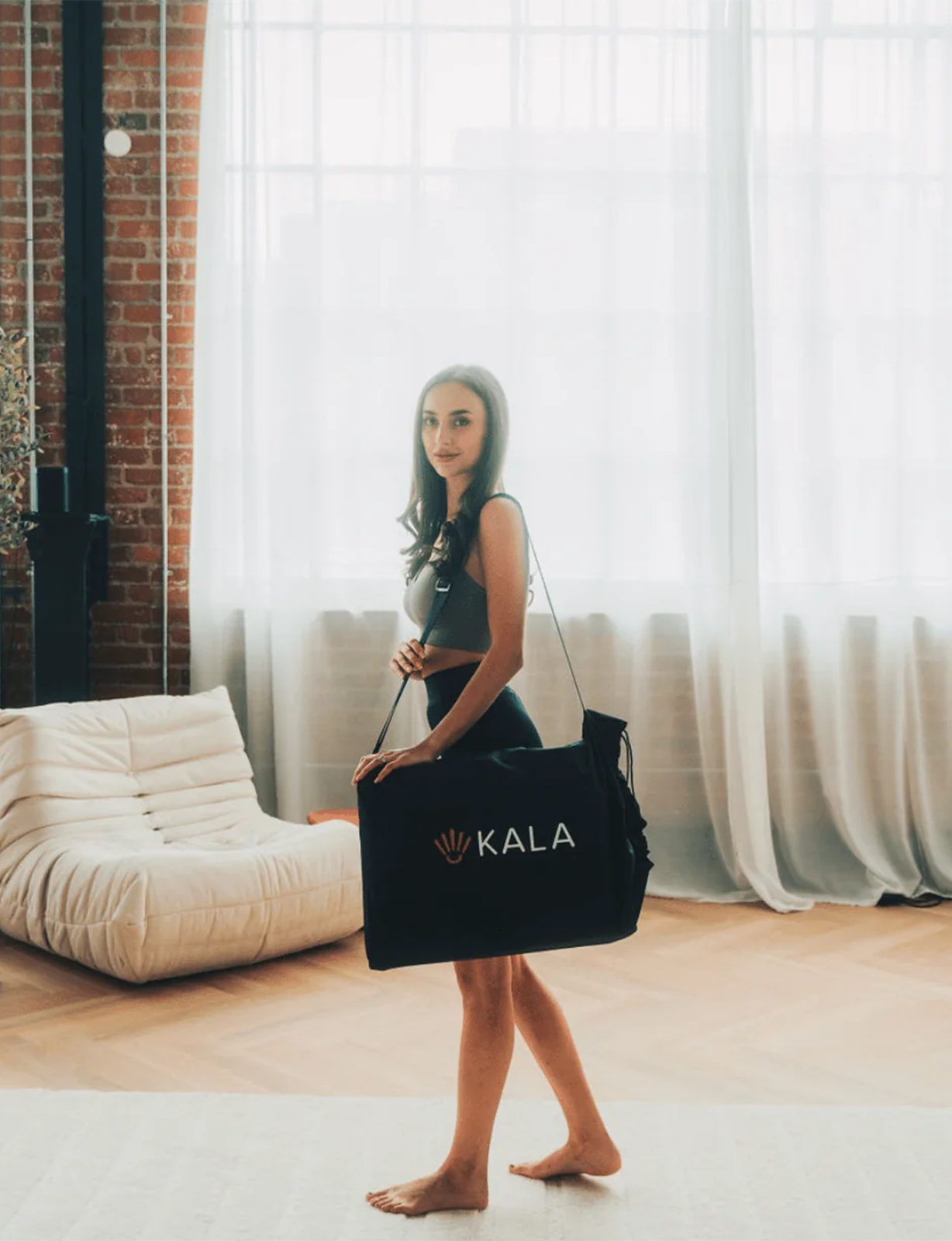 Woman holding a black duffel bag with KALA Sauna Blanket in a room.