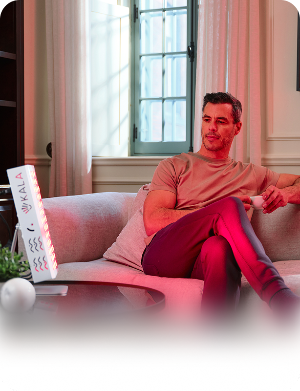 Man relaxing on a sofa in a sitting room while using a KALA Red Light Therapy device, emphasizing comfort and well-being.